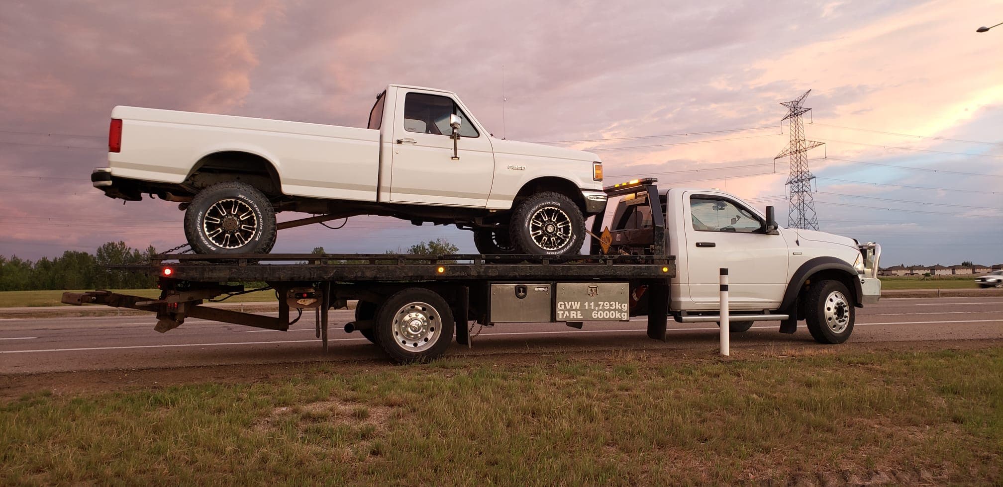 A flatbed tow truck carrying a pickup truck in Edmonton at sunset